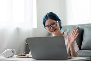 Happy young woman asian using laptop sitting at desk writing notes while watching webinar, studying online, looking at laptop screen learning web classes or having call remote from home photo