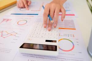 Close up of businessman or accountant hand holding pencil working on calculator to calculate financial data report, photo