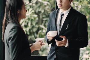 Coffee break. Group business people, standing in modern office, holding a cups, smiling standing at the window photo