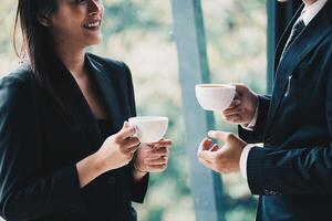 Coffee break. Group business people, standing in modern office, holding a cups, smiling standing at the window photo