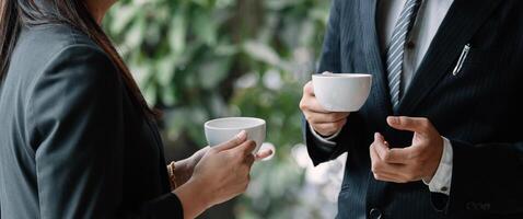 Coffee break. Group business people, standing in modern office, holding a cups, smiling standing at the window photo