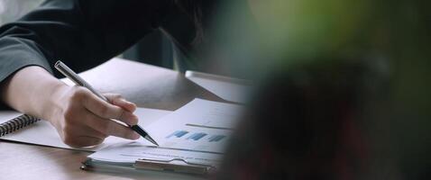 Close up businessman pen pointing turnover with graph chart report and use laptop computer for analysis data photo