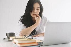 Young attractive woman using laptop while taking note on notepad at office photo