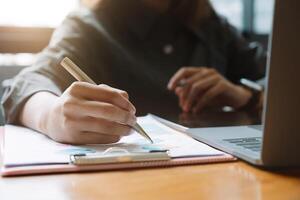 Businessman pen pointing turnover with graph chart report and use laptop computer for analysis data photo
