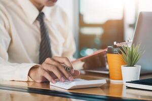Close up of businessman or accountant hand holding pen working on calculator to calculate business data, accountancy document and laptop computer at office, business concept photo