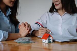 Cropped image of real estate agent assisting client to sign contract paper at desk with house model photo