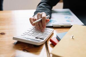 Close up of businesswoman or accountant hand holding pencil working on calculator to calculate financial data report, accountancy document and laptop computer at office, business concept photo