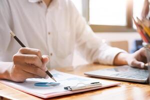 Businessman pen pointing turnover with graph chart report and use laptop computer for analysis data photo
