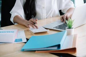 Close up of businesswoman or accountant hand holding pen working on calculator to calculate business data, accountancy document and laptop computer at office, business concept photo