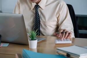 Businessman or accountant working on calculator to calculate business data, accountancy document and laptop computer at office, business concept photo