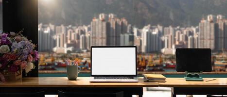 Mockup laptop computer with blank white screen on workplace, cargo port and building background photo