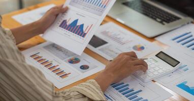 Close up of businessman or accountant hand holding pen working on calculator to calculate business data, accountancy document and laptop computer at office, business concept. photo