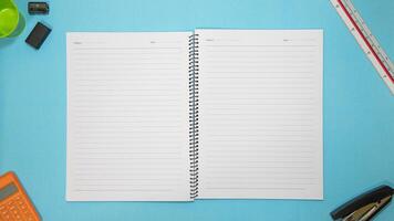 Office table desk with set of colorful supplies, blue blank note pad, cup, pen, pc, crumpled paper, flower on blue background. Top view and copy space for text. photo