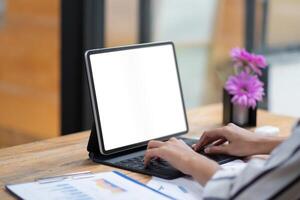 Close up view of female hands typing on a digital tablet keyboard with blank white screen on the wooden desk photo