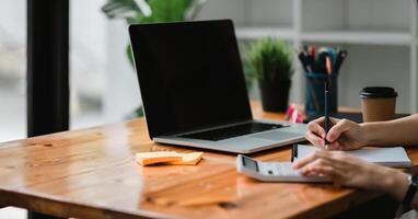 Close up of businessman or accountant hand holding pen working on calculator and laptop computer to calculate business data during make note at notepad, accountancy document at office. photo
