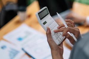 Woman entrepreneur using a calculator with a pen in her hand, calculating financial expense with working desk background photo