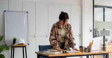 Asian woman working of Architect sketching project on blueprint at site construction work. Concept of architect, engineer in the office desk construction project photo
