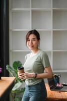 Asian woman standing on front of office workplace while hand holding a cup of coffee and looking outside photo