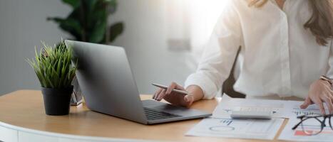Businesswoman using calculator and laptop computer for analysis maketing plan, Accountant calculate financial report, computer with graph chart. Business, Finance and Accounting concept photo