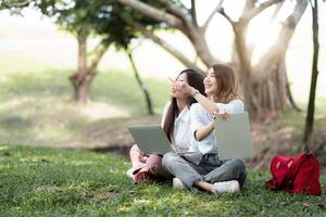 Happy asian university sitting outside on campus. two girl working and studying together with laptop and digital tablet in the park photo