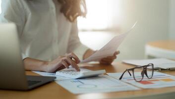 Businesswoman or accountant working Financial Manager Researching Process accounting calculate with calculator for analyse market graph data stock information review on the table in office. photo
