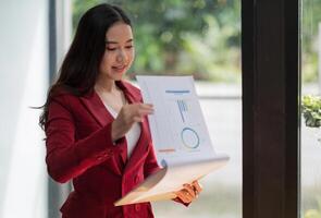 Smiling asian woman standing while checking financial report at office photo