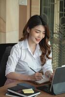 Portrait charming asian woman taking note on notepad while conference via digital tablet photo