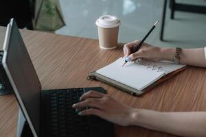 Closd up business woman taking note on paper with and she is using a laptop computer on a wooden desk in the office. Web banner photo