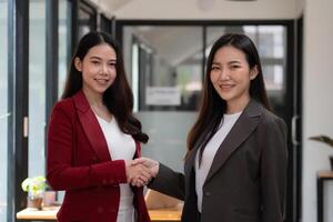 Two confident business asian woman shaking hands during looking at camera in the office, success, dealing, greeting and partner concept photo