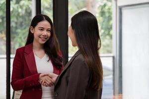 Smiling young businesswoman shaking hands with a coworker during a meeting with colleagues around a table in an office. photo