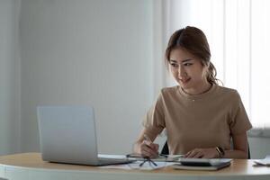 portrait of smiling woman making notes while taking part in webinar at tabletop with laptop in office photo