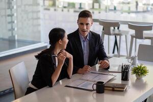 Asian and caucasian businesspeople learn new business app, apprentice listen associate tell about corporate program. Multiracial client and bank manager at business meeting using laptop negotiating photo