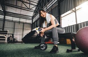 atractivo aptitud mujer sentado en un silla y descansando después rutina de ejercicio a aptitud centro. hembra tomar un descanso después difícil cardio foto