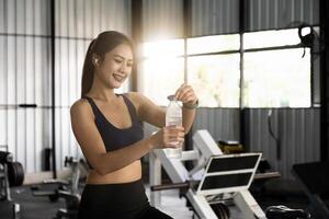 asiático joven mujer Bebiendo agua después rutina de ejercicio en gimnasia, saludable y deporte concepto. foto