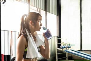 joven asiático atlético mujer Bebiendo agua después rutina de ejercicio o ejercicio en aptitud gimnasia. foto
