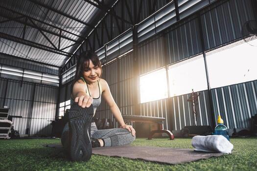 joven asiático hembra en elegante y confortable ropa de deporte extensión su piernas en el aptitud piso. ejercicio y deporte concepto. ajuste mujer haciendo extensión rutina de ejercicio a gimnasio foto
