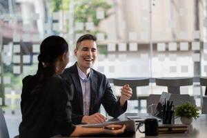 Asian and caucasian businesspeople learn new business app, apprentice listen associate tell about corporate program. Multiracial client and bank manager at business meeting using laptop negotiating photo