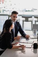 Multiethnic male caucasian mentor and female asian sitting at desk with laptop doing paperwork together discussing project financial report. Corporate business collaboration concept photo