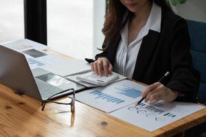 Close up of businesswoman or accountant hand holding pen working on calculator to calculate business data, accountancy document and laptop computer at office, business concept. photo