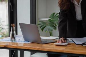 Close up of business woman or accountant hand holding pen working on calculator to calculate business data, accountancy document and laptop computer at office, business concept. photo