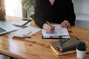Businesswoman discussing analysis charts or graphs on desk table and using laptop computer. Close up female analysis and strategy concept photo