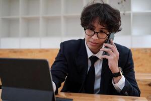 Portrait of asian business man young smiling cheerful entrepreneur in casual office making phone call while working with digital tablet photo