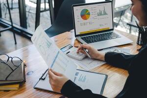Business woman using calculator for analysis maketing plan, Accountant calculate financial report, computer with graph chart. Business, Finance and Accounting concept photo