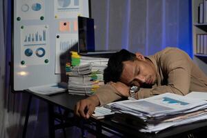 Exhausted businessman sleeping at his desk and working overtime late at night, he is surrounded by piles of paperwork photo