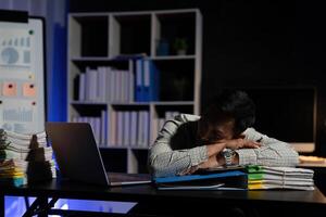 Exhausted businessman sleeping at his desk and working overtime late at night, he is surrounded by piles of paperwork photo