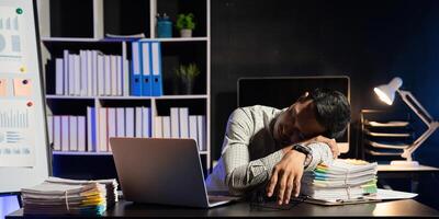 Exhausted businessman sleeping at his desk and working overtime late at night, he is surrounded by piles of paperwork photo