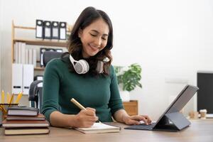 Smiling girl student wear headphone study online with laptop computer, happy young woman learn language listen lecture watch webinar write notes look at laptop sit in cafe, distant education photo