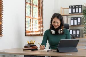 Smiling girl student wear headphone study online with laptop computer, happy young woman learn language listen lecture watch webinar write notes look at laptop sit in cafe, distant education photo