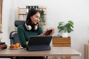 Smiling girl student wear headphone study online with laptop computer, happy young woman learn language listen lecture watch webinar write notes look at laptop sit in cafe, distant education photo