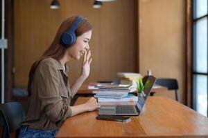Asian tutor of language start online lesson with trainee wave hand smiling looks at pc screen. woman in headphones communicating distantly, e-learning process, application usage concept photo